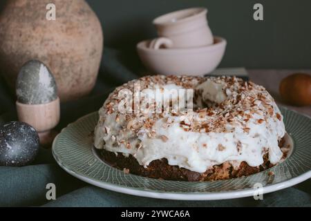 Bundt cake decorated with icing and chopped nuts on a plate next to painted Easter eggs and assorted crockery Stock Photo