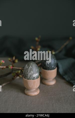 Close-up of two painted Easter eggs in wooden egg cups on a table next to cherry blossom branches Stock Photo