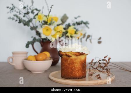 Easter sponge cake with buttercream icing on a table with fresh eggs and a bunch of daffodils in a jug Stock Photo
