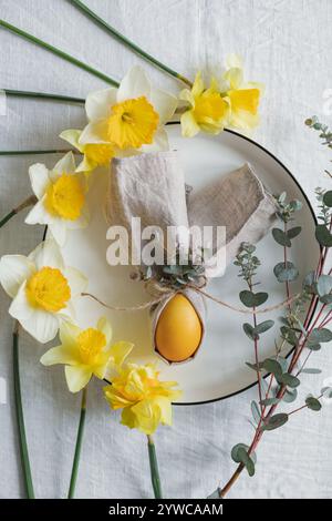 Overhead view of an Easter place setting with an Easter egg in a napkin folded into the form of rabbit ears and yellow daffodils Stock Photo