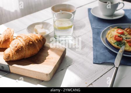 Close-up of a cheese, cherry tomato and spinach omelette with baked beans, croissants, black coffee and lemon water Stock Photo