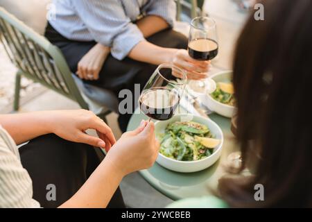 Close-up of three women enjoying a glass of red wine while having lunch on a summer terrace Stock Photo