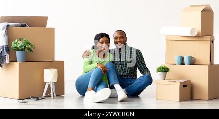 New Property. Cheerful Black Couple Sitting Among Unpacked Belongings After Moving Stock Photo