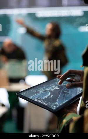 Army staff monitoring infantry unit on ongoing operation using his tablet, using surveillance radar system and a world map. IT professional working with reconnaissance gear. Close up. Stock Photo