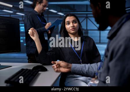Teamworking programmers in data center using diagnostic tools and system monitoring software to identify root cause of errors. Multiethnic team in server farm repairing equipment together Stock Photo