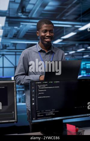 Smiling engineer pleased by recovery plan, monitoring data center energy consumption. Happy african american employee in server room making sure sensors are functioning optimally, doing disk checks Stock Photo