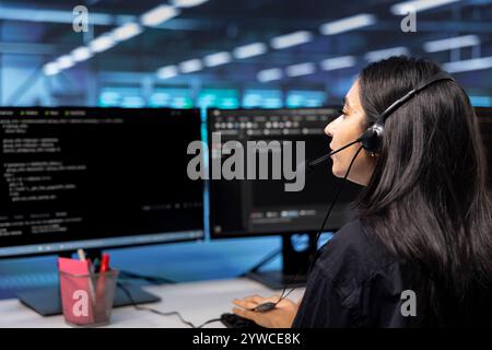 IT support personnel in data center talking in headphones microphone, doing checkup. Woman at work in server hub chatting with on field engineer, monitoring servers infrastructure Stock Photo