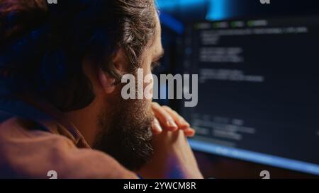 Programmer in home office concentrating on finding bugs while doing coding on computer, extreme close up shot. IT admin frowning while looking at screen, confused by errors in lines of code, camera B Stock Photo
