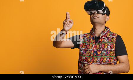 Indian man wearing virtual reality headset, doing swiping gestures. Technology enthusiast using high tech futuristic modern VR gadget, isolated over studio background, camera A Stock Photo