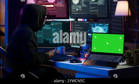 Green screen laptop used by hacker in underground hideout to write lines of code, developing virus that get past security systems. Chroma key device used by evil developer in hidden bunker, camera A Stock Photo