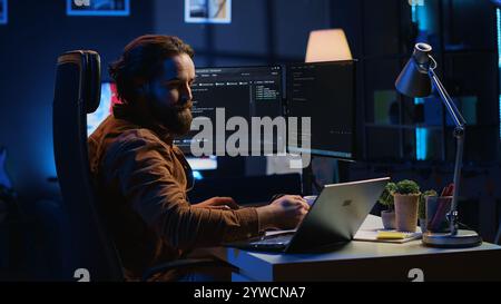 Software programmer putting headphones on while developing code, making time pass faster during remote job shift. IT professional doing multitasking in apartment office while listening music, camera A Stock Photo