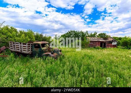 An old truck is parked in a field next to a dilapidated house. The scene is quiet and peaceful, with the only sounds being the rustling of the grass a Stock Photo