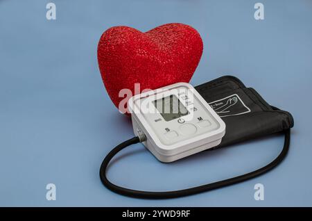 White electric tonometer on a blue background with heart. Pressure measuring apparatus. Stock Photo