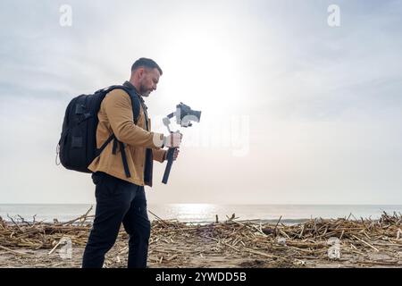 Videographer walking on the beach using his camera with a gimbal to record the environmental disaster caused by the flood Stock Photo