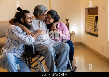 Happy Indian young couple spending time with disabled father on wheel chair at home. Happy parents Day. Stock Photo