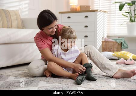 Mother helping her daughter to put tights on at home Stock Photo