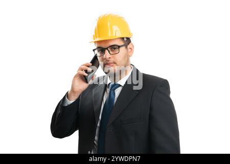Architect or contractor man with serious expression wearing yellow helmet for safety speaking on phone isolated on white studio background Stock Photo