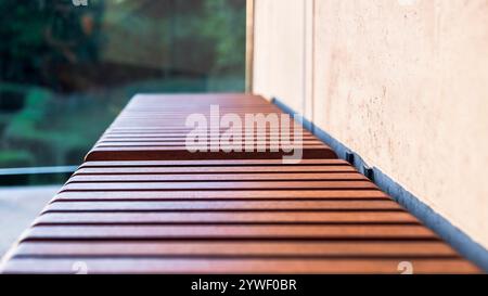 Wooden slats on the bench seat. Exotic Iroko wood. Detail. Close up. Architectural concrete wall and greenery in the background Stock Photo