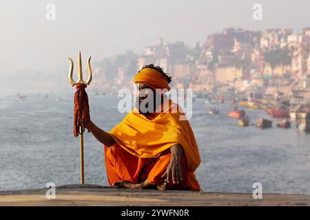 Hindu holy man with the trident of Hindu God Shiva with the River Ganges in the background in Varanasi, India Stock Photo