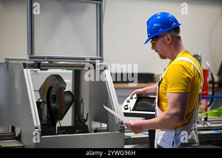 Factory worker wearing safety glasses and hardhat operating industrial saw and reading instructions. Stock Photo