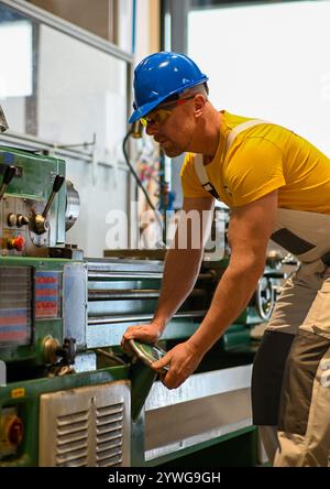 Skilled metalworker operating a lathe machine, producing precision parts in a factory workshop. Stock Photo