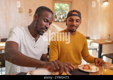 Two African American LGBT couple having breakfast, tasting fresh fruit and vegetables, enjoying delicious healthy food taste in a hotel accommodation. Stock Photo