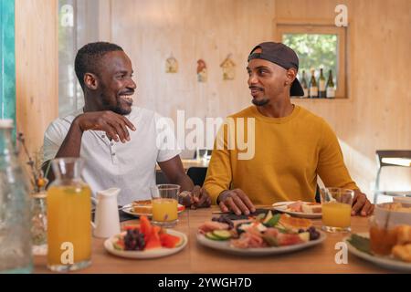 Two African American male friends on vacation abroad, enjoying tasty breakfast in a glamping resort restaurant. Gourmet tourism concepts. Stock Photo