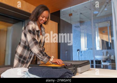 Smiling young woman packing her suitcase in a hotel room, returning home after a successful business trip. Stock Photo