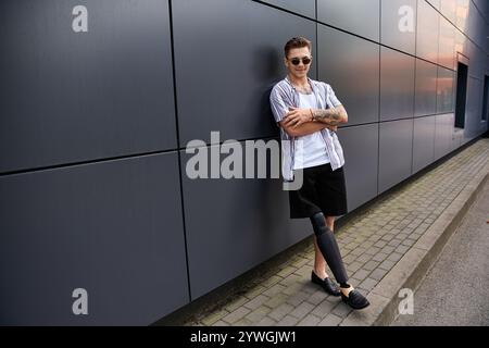 Young man with a prosthetic leg poses with confidence near a sleek urban building. Stock Photo