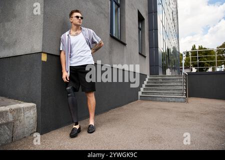 Young man with a prosthetic leg poses stylishly against an urban backdrop on a sunny day. Stock Photo