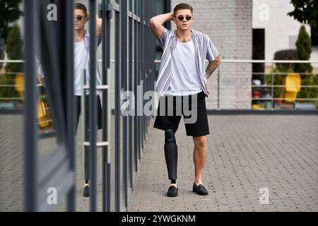 Handsome young man with a prosthetic leg poses confidently near modern glass architecture. Stock Photo