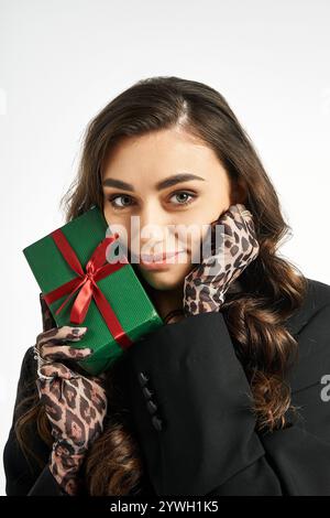 A beautiful young woman smiles while holding a green gift adorned with a red ribbon. Stock Photo