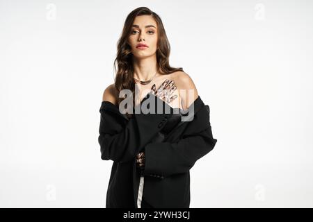 Young woman poses confidently in a black oversized coat, highlighting her stylish hand tattoos. Stock Photo