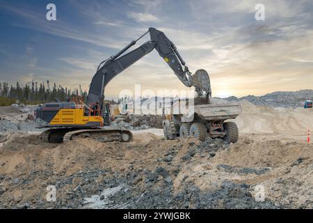 An excavator loads a dump truck with soil at sunset on a construction site Stock Photo