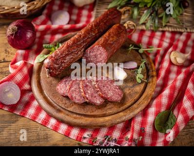 Sliced salami on wooden board with herbs and red onions Stock Photo