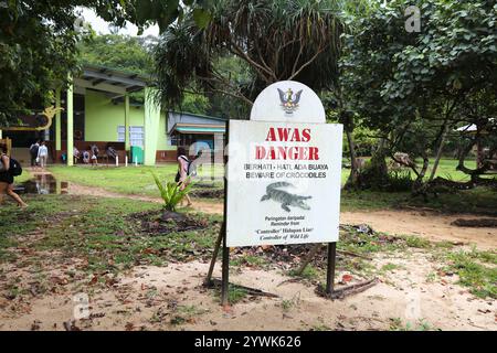 BAKO NATIONAL PARK, MALAYSIA - MARCH 9, 2024: Tourists walk by crocodile warning sign in Bako National Park in Sarawak state of Borneo island, Malaysi Stock Photo