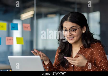 Businesswoman communicating during an online meeting, utilizing technology for effective collaboration. She is surrounded by notes, focusing on professional tasks in a modern office Stock Photo