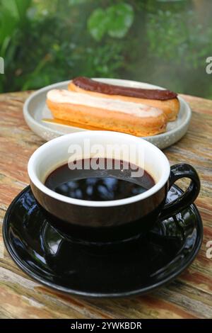 A Cup of Hot Coffee with Blurry Chocolate and Vanilla Eclairs in the Backdrop Stock Photo
