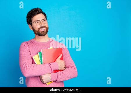 Confident man holding colorful notebooks against blue background, expressing thoughtful and cheerful mood Stock Photo