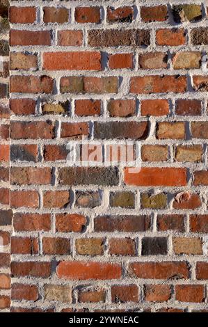 Textured brick wall features a diverse mix of colors including reds and browns, creating a rustic appearance perfect for adding charm to any space Stock Photo