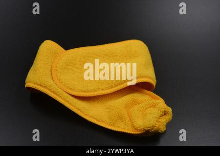 An unusual cleaning cloth, a long yellow microfiber set on a black, matte plastic background. Stock Photo