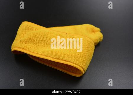 An unusual cleaning cloth, a long yellow microfiber set on a black, matte plastic background. Stock Photo