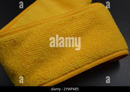 An unusual cleaning cloth, a long yellow microfiber set on a black, matte plastic background. Stock Photo