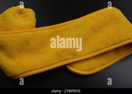 An unusual cleaning cloth, a long yellow microfiber set on a black, matte plastic background. Stock Photo