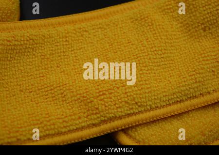 An unusual cleaning cloth, a long yellow microfiber set on a black, matte plastic background. Stock Photo