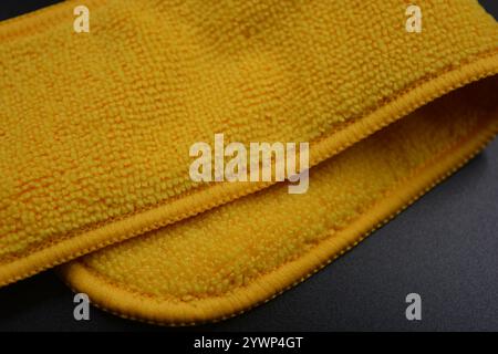 An unusual cleaning cloth, a long yellow microfiber set on a black, matte plastic background. Stock Photo