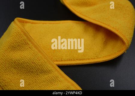 An unusual cleaning cloth, a long yellow microfiber set on a black, matte plastic background. Stock Photo