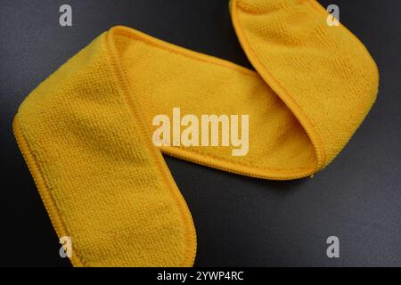 An unusual cleaning cloth, a long yellow microfiber set on a black, matte plastic background. Stock Photo
