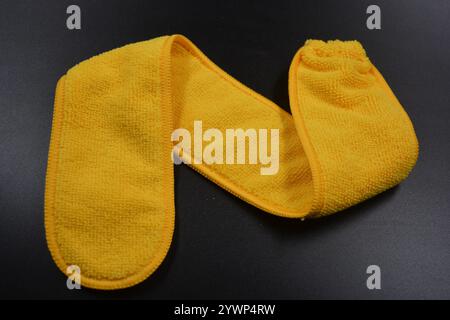 An unusual cleaning cloth, a long yellow microfiber set on a black, matte plastic background. Stock Photo