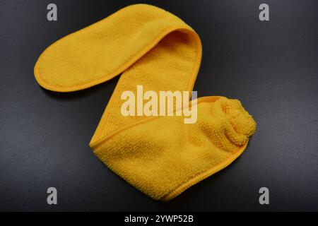 An unusual cleaning cloth, a long yellow microfiber set on a black, matte plastic background. Stock Photo